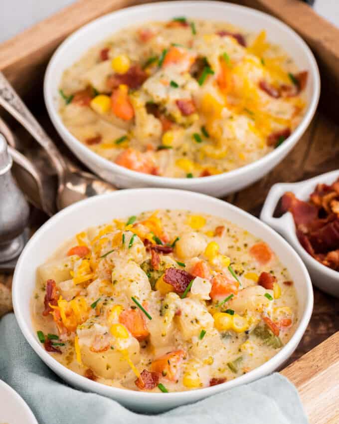 two bowls of creamy vegetable soup on a serving tray with a linen napkin, two spoons, and bacon as a topping