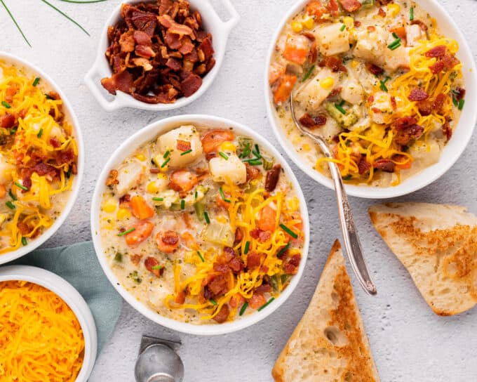 overhead view of several bowls of creamy vegetable soup with cheese and bacon as toppings