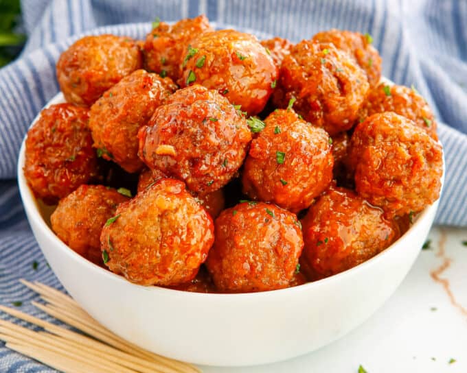 pile of buffalo crockpot meatballs in a white bowl on table with blue napkin and toothpicks