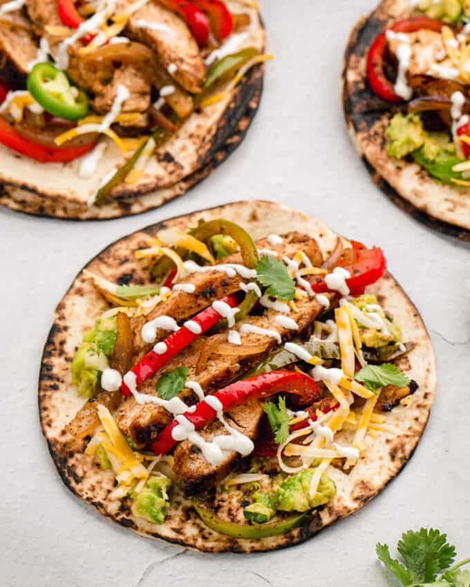 three charred flour tortillas filled with chicken fajitas and sour cream