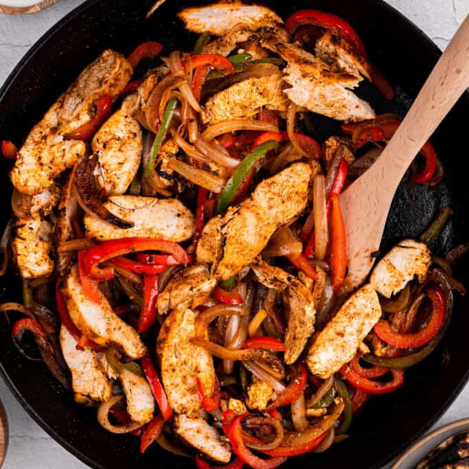 overhead view of chicken fajitas in cast iron skillet with a wooden spoon