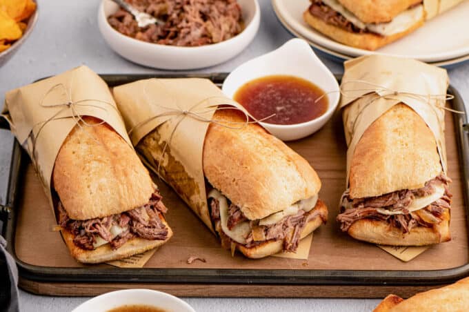 serving tray with three french dip sandwiches wrapped in paper
