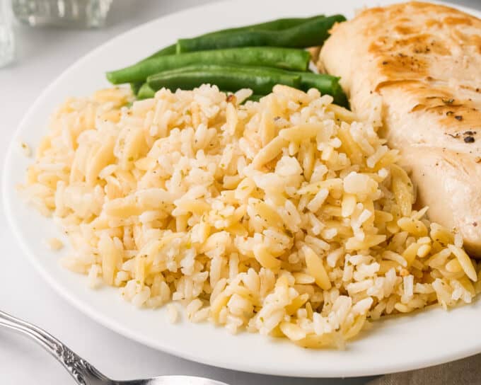 serving of rice pilaf on a white plate with a chicken breast and green beans