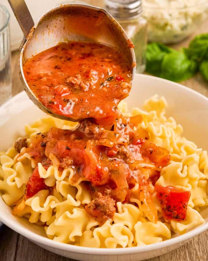 pouring a ladle of lasagna soup over cooked noodles in a white bowl