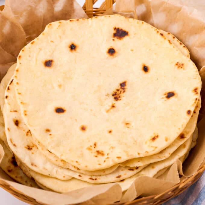 stack of flour tortillas in a basket with parchment paper