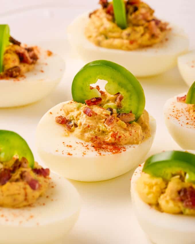 bacon jalapeño deviled eggs on white plate garnished with a jalapeño slice