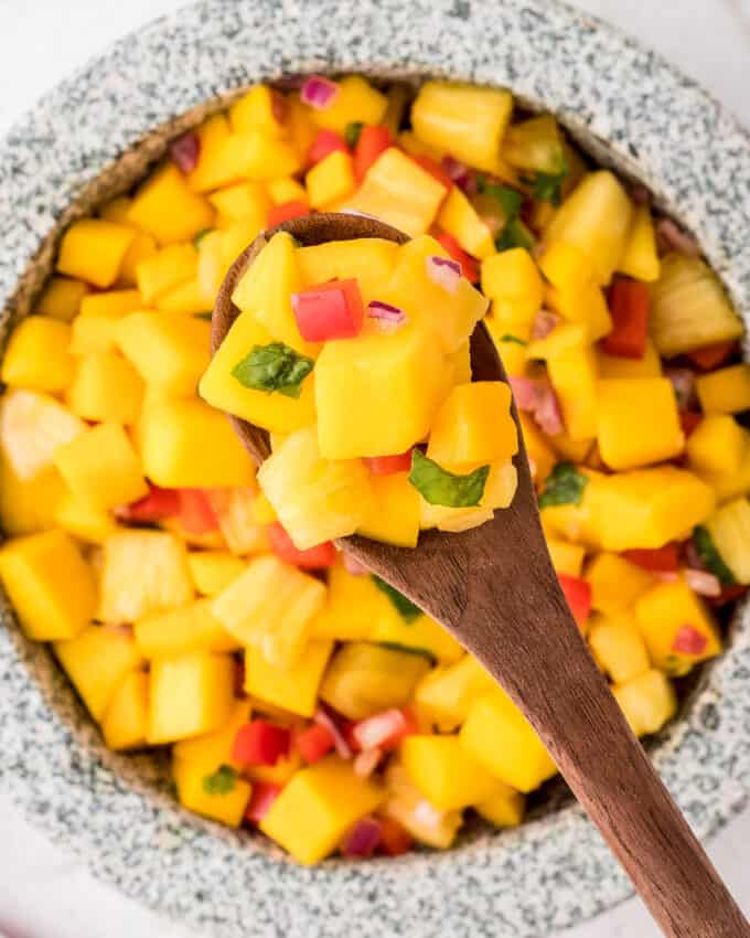 bowl of mango salsa with a wooden spoon serving it