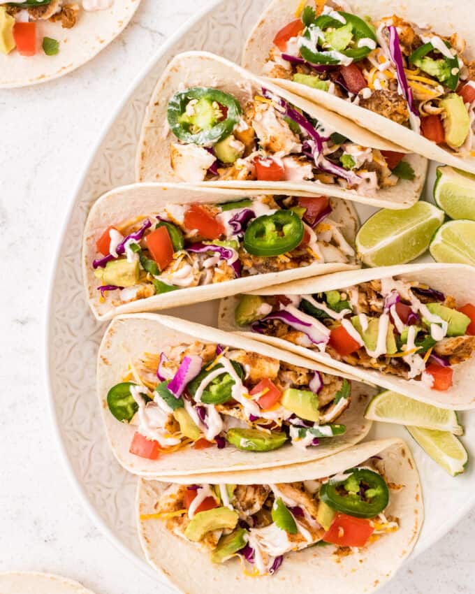 fish tacos on a white platter with lime wedges