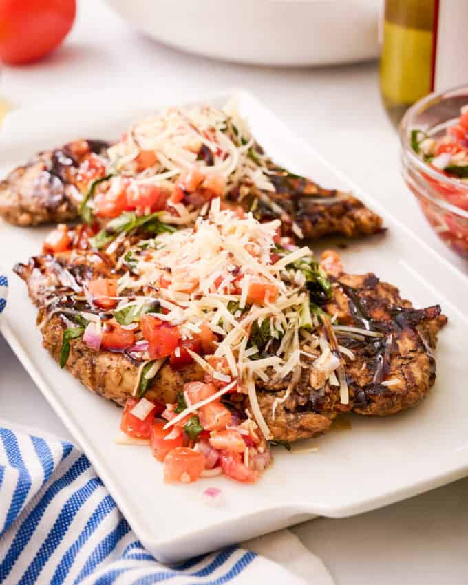 grilled chicken breasts topped with a tomato bruschetta topping on a white platter
