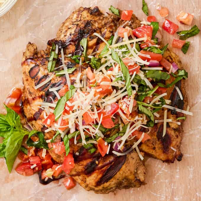 overhead photo of two grilled chicken breasts topped with tomato bruschetta, herbs, and Parmesan cheese