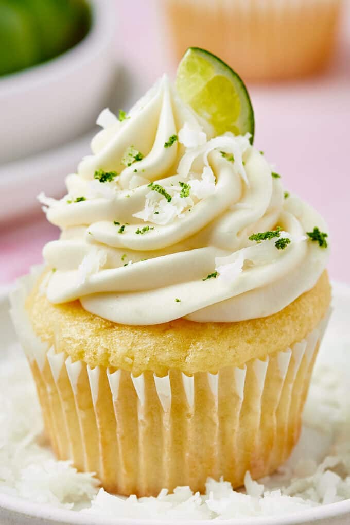 side view photo of a coconut cupcake garnished with lime frosting, lime zest, shredded coconut, and a lime slice