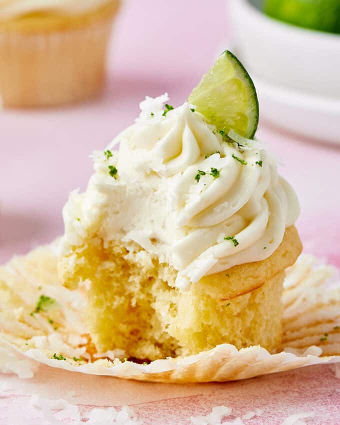 photo of a coconut cupcake with a bite taken out of it, on a pink table.