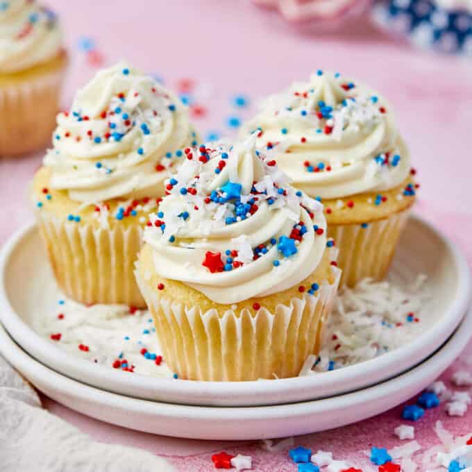 stack of two white plates topped with three coconut cupcakes decorated with red white and blue sprinkles