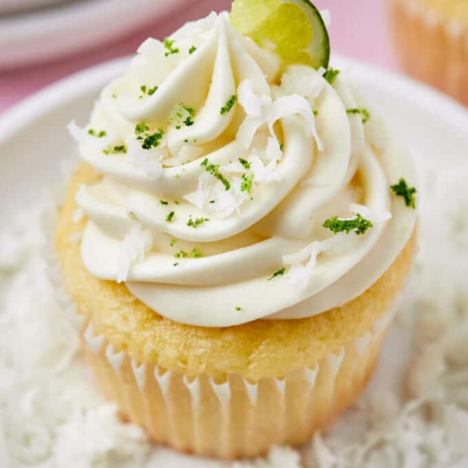 angled photo showing lime coconut cupcake on a white plate sprinkled with coconut and lime zest