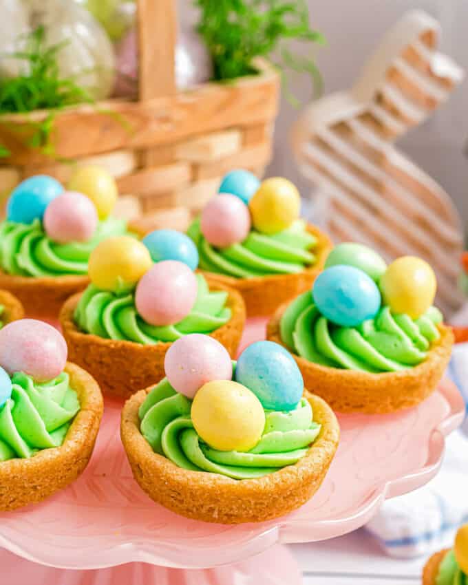 sugar cookie cups decorated for Easter on a cake stand with Easter decorations around it