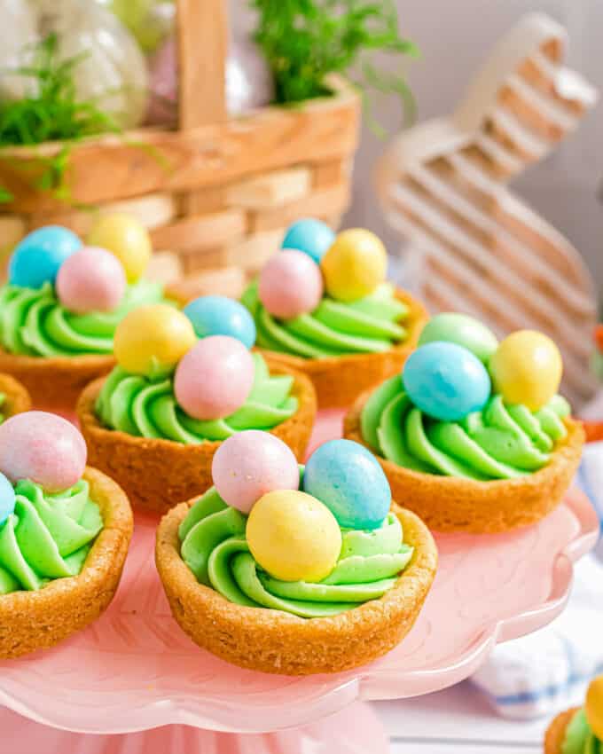 sugar cookie cups decorated for Easter on a cake stand with Easter decorations around it