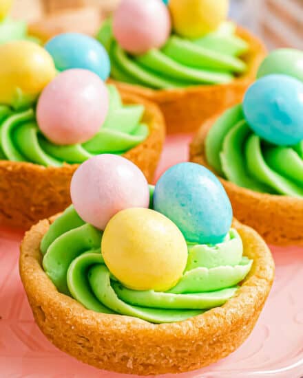 These Sugar Cookie Cups are made with pre-made dough baked in muffin pans, then pressed down to create a cup. Filled with a silky buttercream frosting, these sweet and chewy cookie cups are then topped with Easter/Spring candies to make a fun and festive Spring dessert!