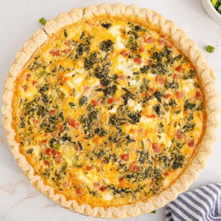 overhead photo of a ham and cheese quiche on a marble countertop with a blue and white striped napkin