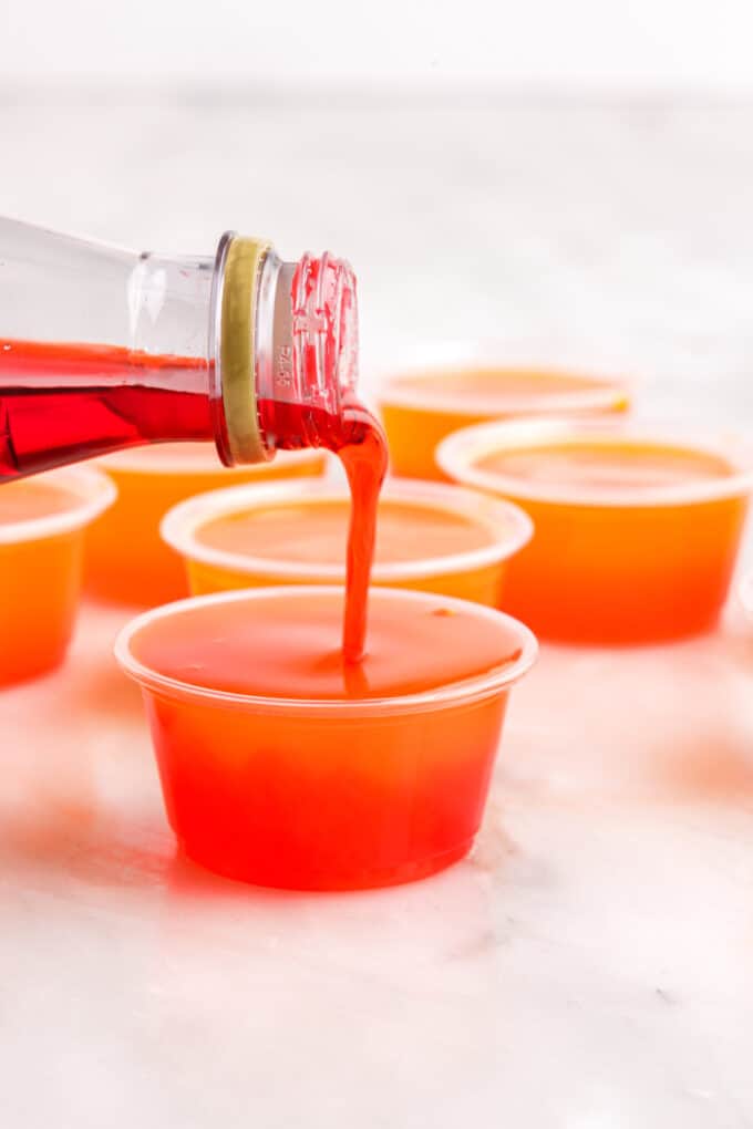 pouring grenadine into a tequila sunrise jello shot before it's set