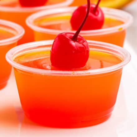 photo of multiple tequila sunrise jello shots on a white plate, garnished with a cherry
