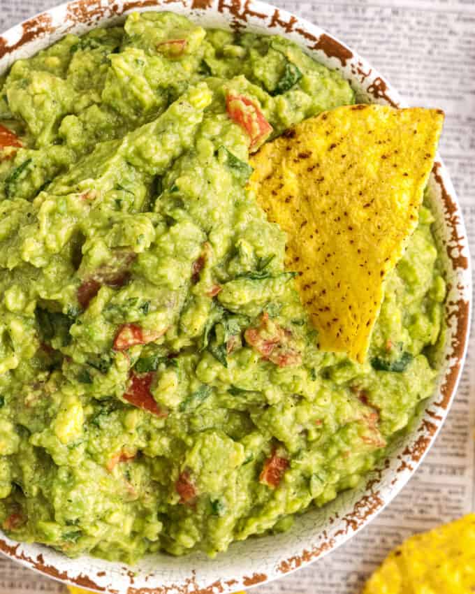 overhead photo of a white bowl of guacamole with a chip dipped into it