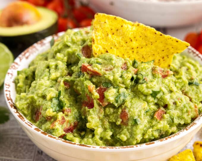 dipping a tortilla chip into guacamole with tomatoes.