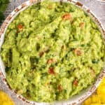 overhead photo of a distressed white bowl full of guacamole with tomatoes