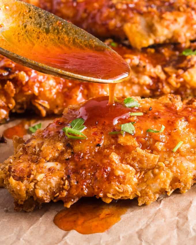 drizzling a breaded chicken tender with hot honey sauce.