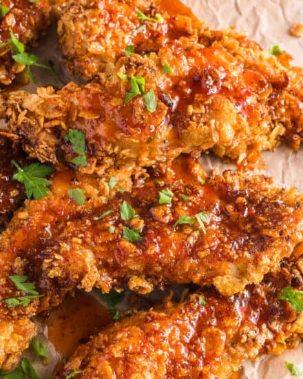 Juicy chicken tenders are coated with a crunchy cornflake breading, air fried until perfectly golden, then liberally drizzled with a sweet and spicy homemade hot honey sauce!