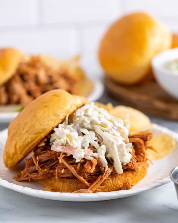 pulled pork sandwich topped with coleslaw on a brioche bun on white plate.