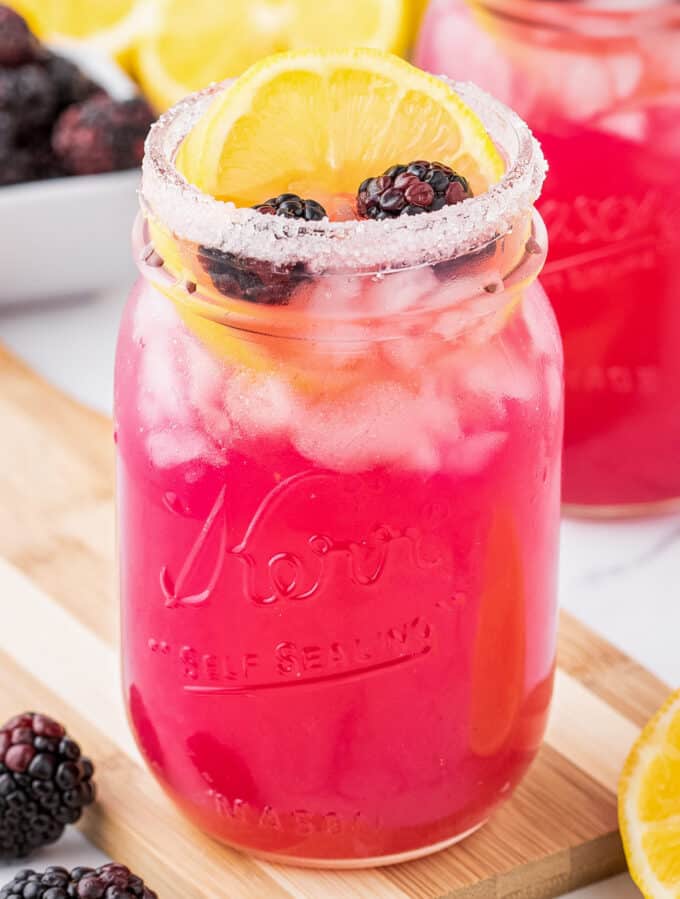 glass jar of blackberry lemonade on wooden cutting board with blackberries and lemon slices