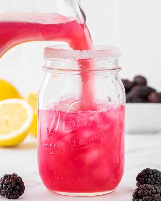 pouring blackberry lemonade into a glass mason jar with ice.