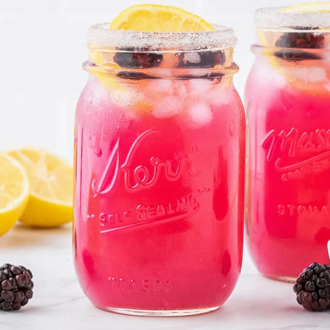 two mason jars of blackberry lemonade garnished with a lemon slice and blackberries