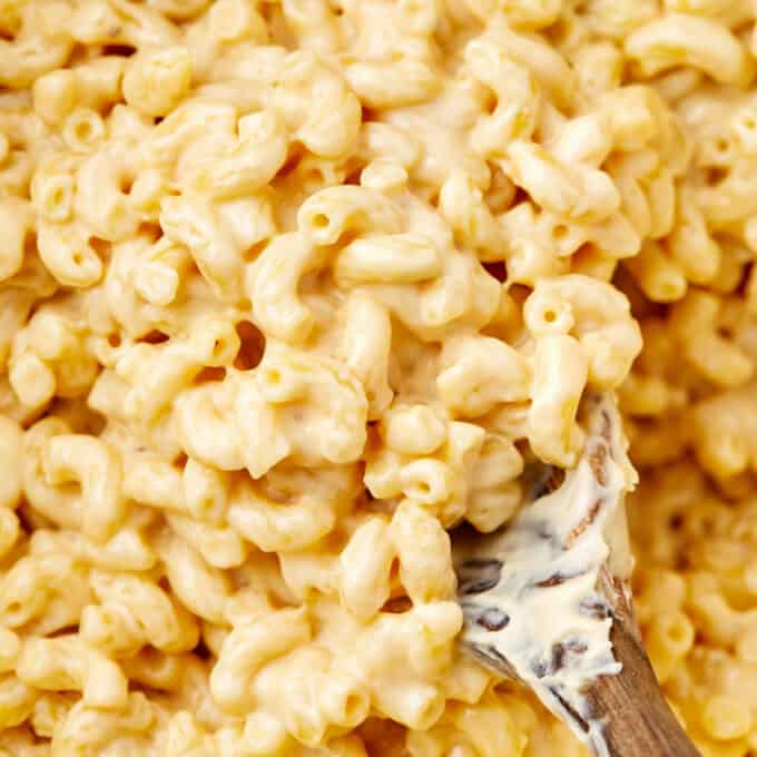 close up photo of macaroni and cheese in a pot on a wooden serving spoon