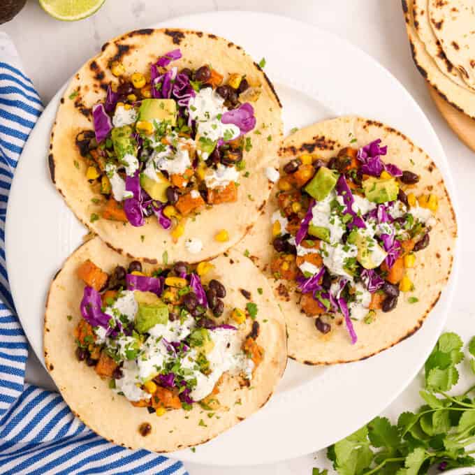 three flour tortillas topped with sweet potato taco filling and lime crema