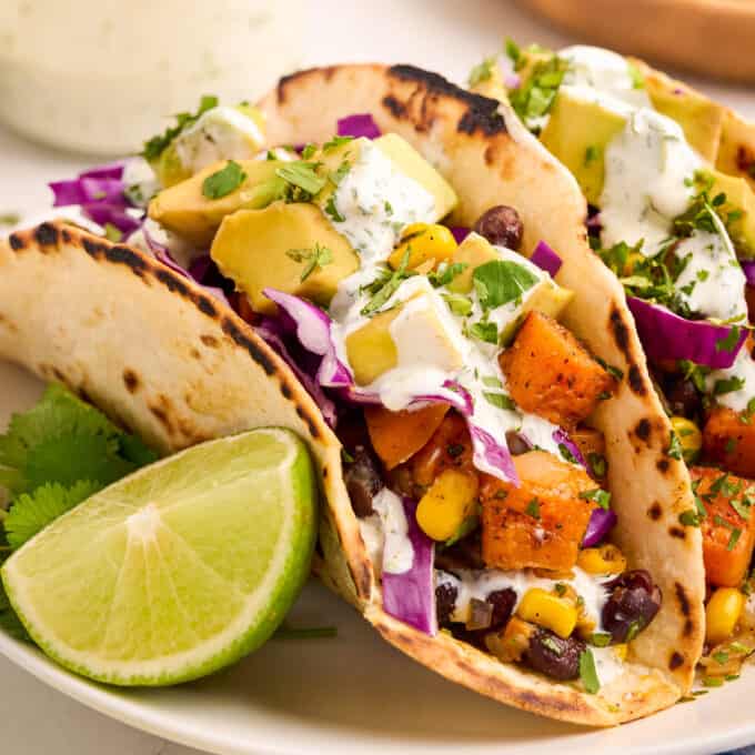 close view of sweet potato tacos on a white plate with a lime wedge and cilantro