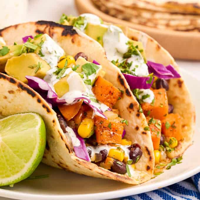 two vegetarian tacos on a white plate with a lime wedge