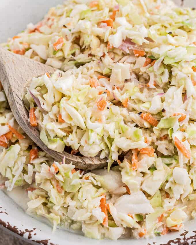 wooden serving spoon scooping coleslaw out of a serving bowl.