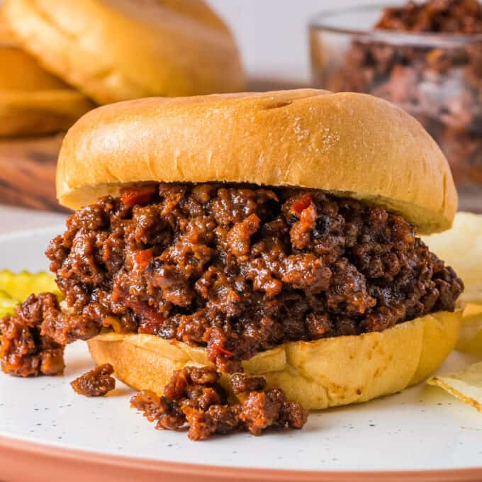 close view of a sandwich bun filled with beef sloppy joes on a white plate.