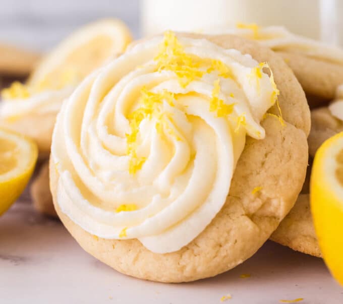 close view of a sugar cookie topped with a swirl of lemon frosting and lemon zest.