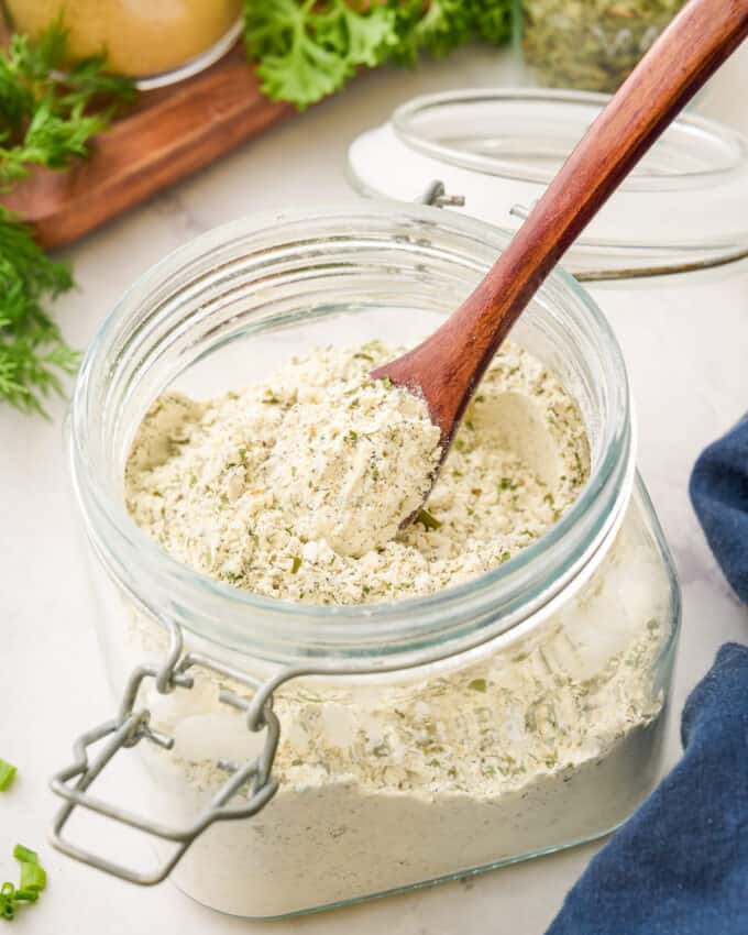 stirring ranch seasoning mix in a glass jar with a small wooden spoon.