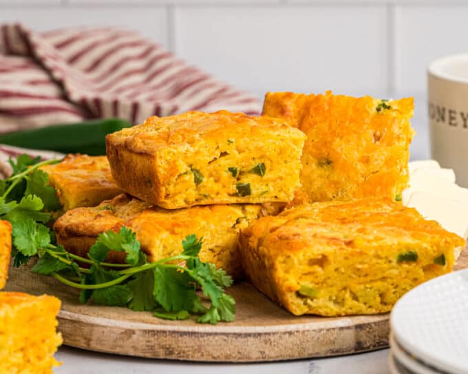 stack of cornbread on a wooden plate on a counter.