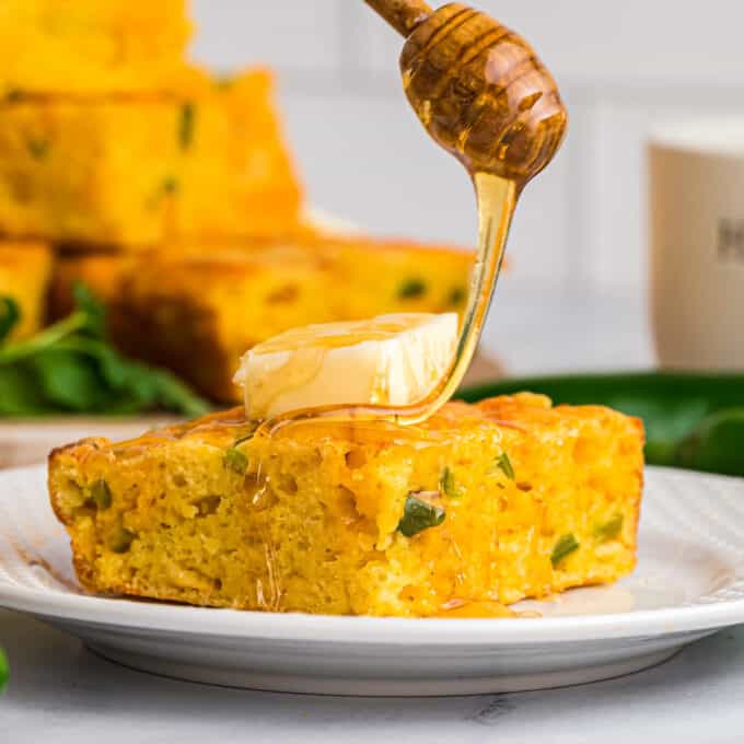 honey being drizzled on a slice of cornbread with butter on top.