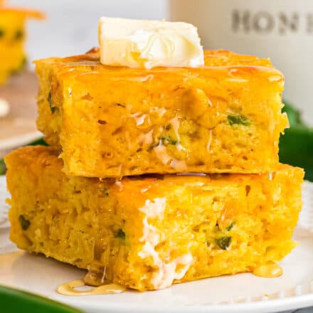 two slices of jalapeno cheddar cornbread stacked on a white plate, topped with butter and honey
