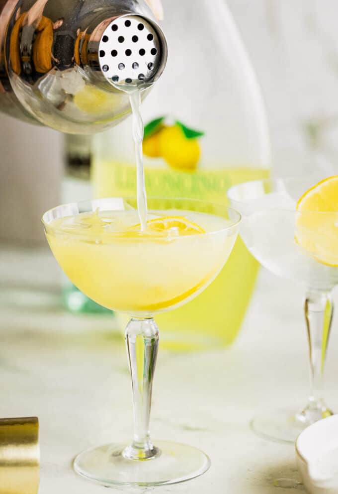 pouring limoncello cocktail into a coupe glass