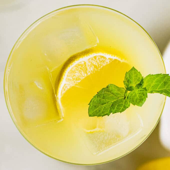 overhead view of lemon cocktail garnished with ice, lemon slice, and fresh mint.