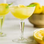 two coupe glasses full of a limoncello cocktail, garnished with lemon slices and fresh mint.