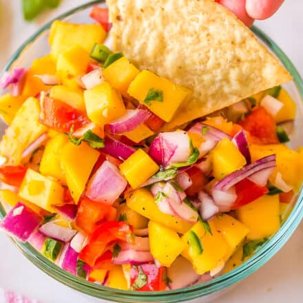 mango salsa in a glass bowl with a tortilla chip being dipped in it.