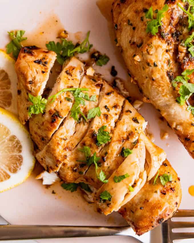 sliced air fried chicken breast on a pink plate, garnished with lemon and parsley.