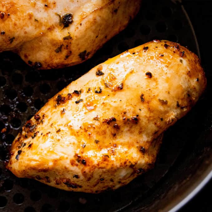 close up photo of two chicken breasts in the basket of an air fryer.